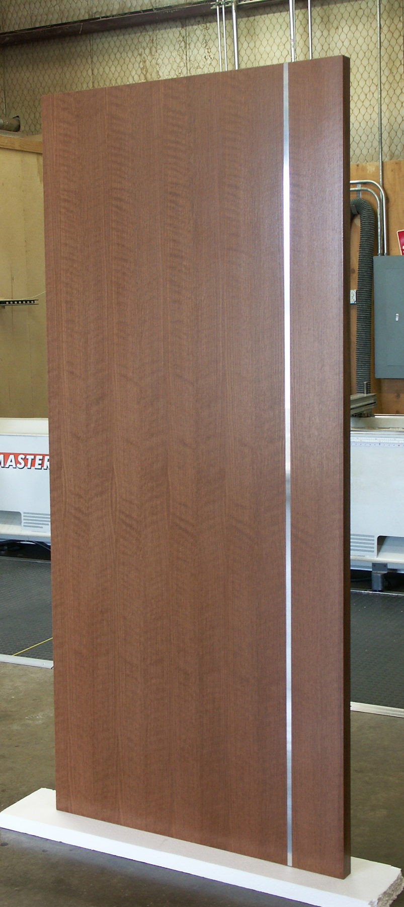Mahogany door with a single vertical stainless steel inlay, standing in the factory
