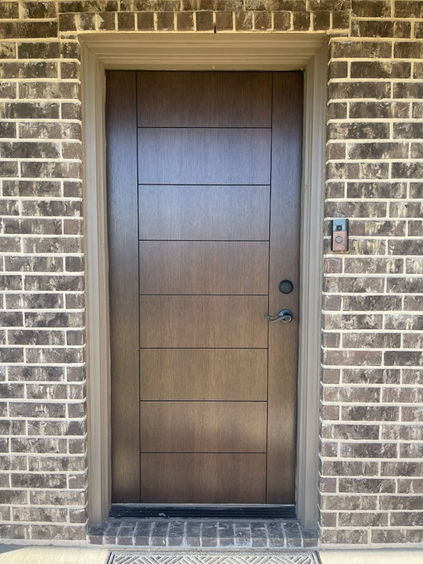 Rift-cut white oak entry door with horizontal grooves, installed in a brick exterior wall