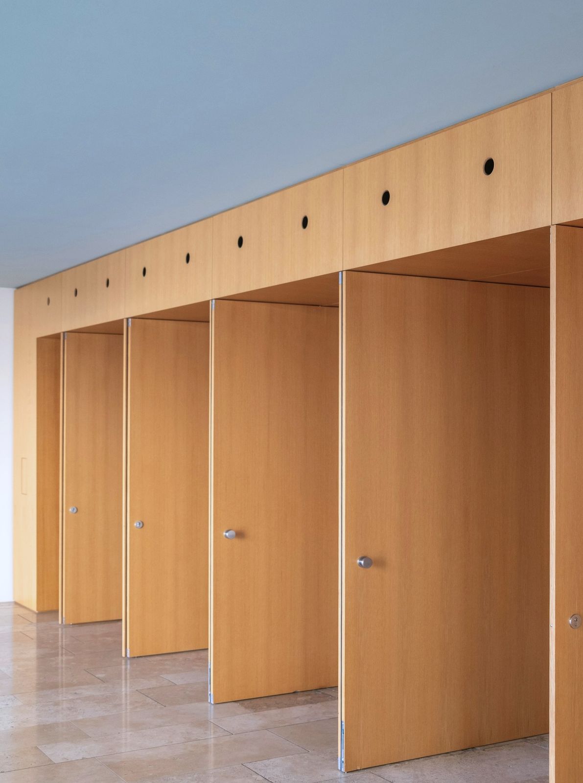 A row of full-height wood veneer doors set into a veneered wall