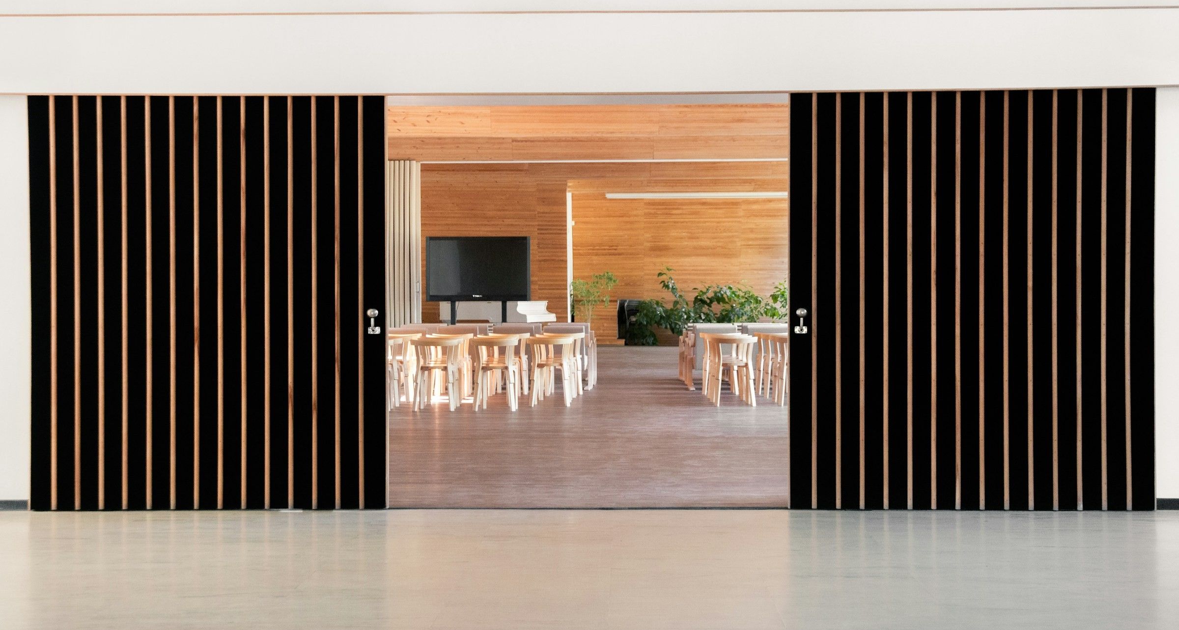 A pair of dark slatted sliding doors opening onto a wood-panelled dining hall